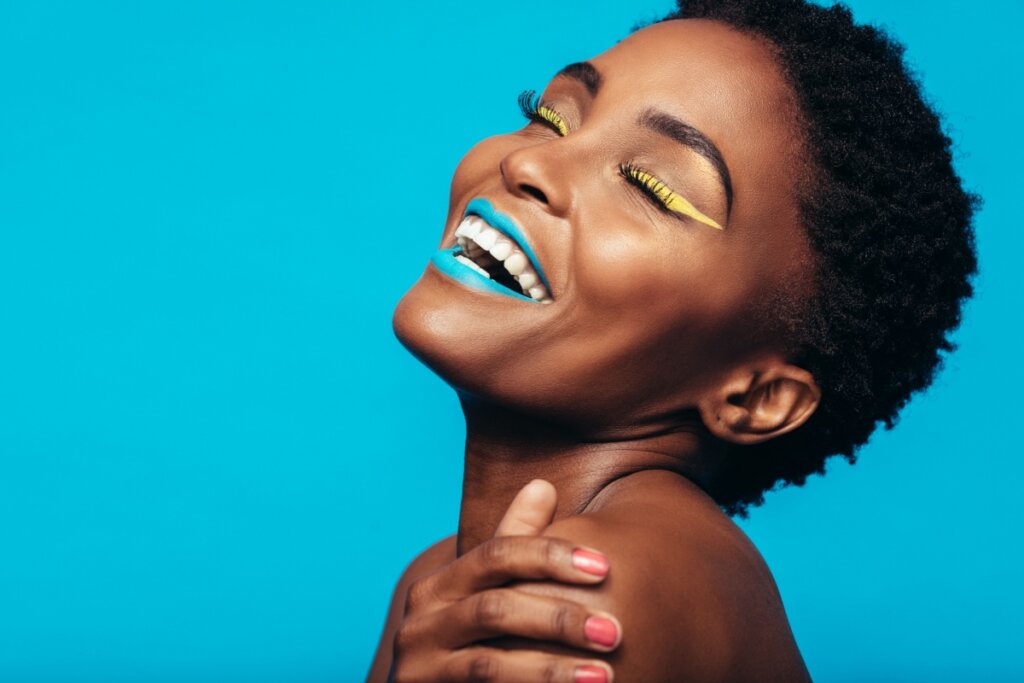 Mulher sorrindo com batom azul e delineado amarelo.