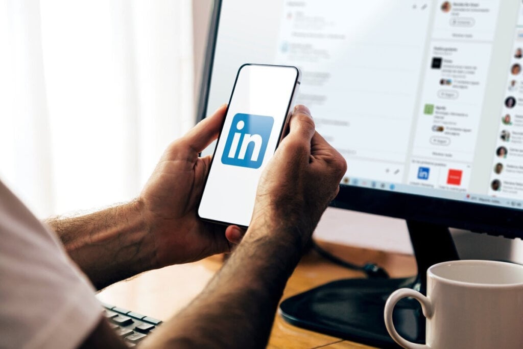 Duas mãos segurando um celular logado no LinkedIn
