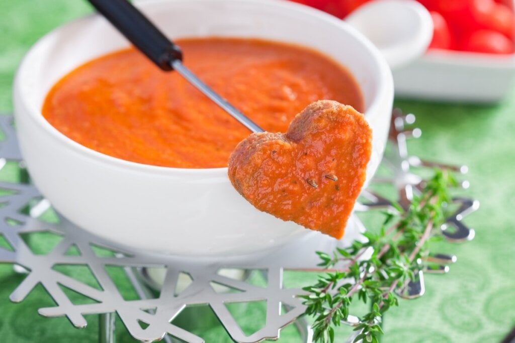 Fondue de tomate em porcelana branca com um pedaço de pão em forma de coração com o fondue 