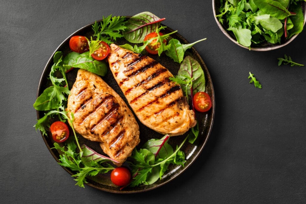 Filé de frango grelhado em prato fundo com folhas verdes e tomate-cereja