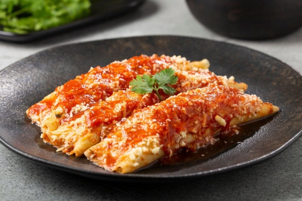 Três panquecas, uma ao lado da outra, com molho de tomate e queijo em cima de prato preto