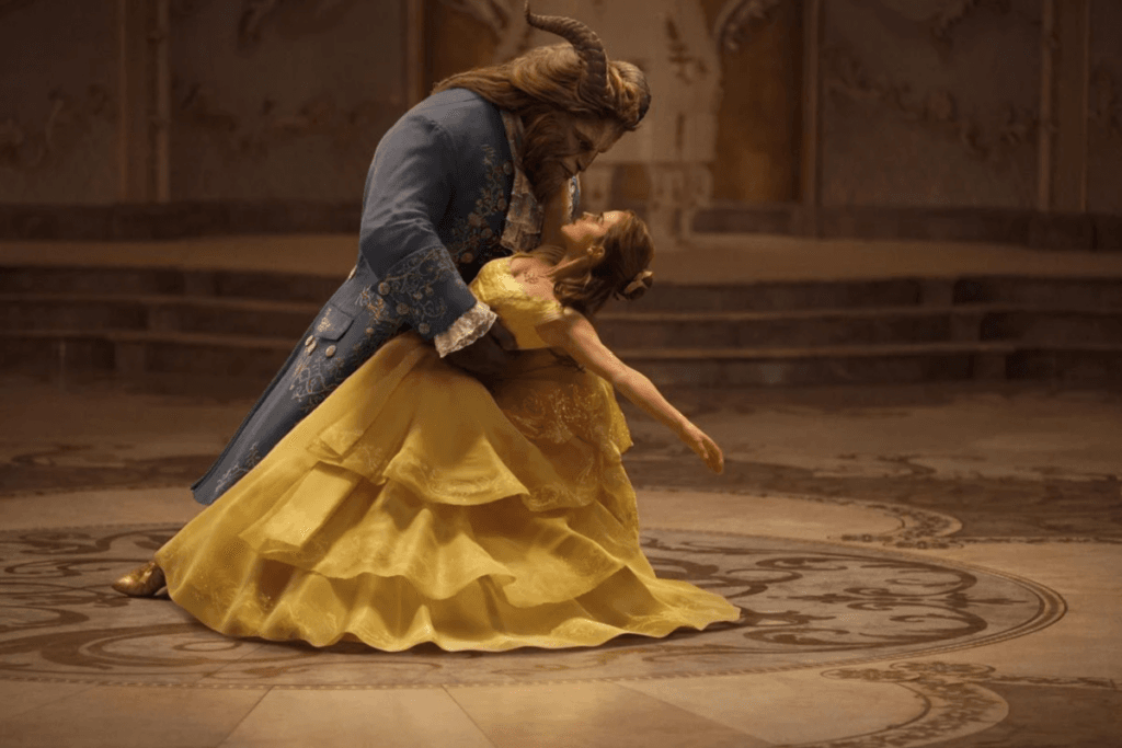 Bela, de vestido amarelo, e a Fera dançando no salão do castelo