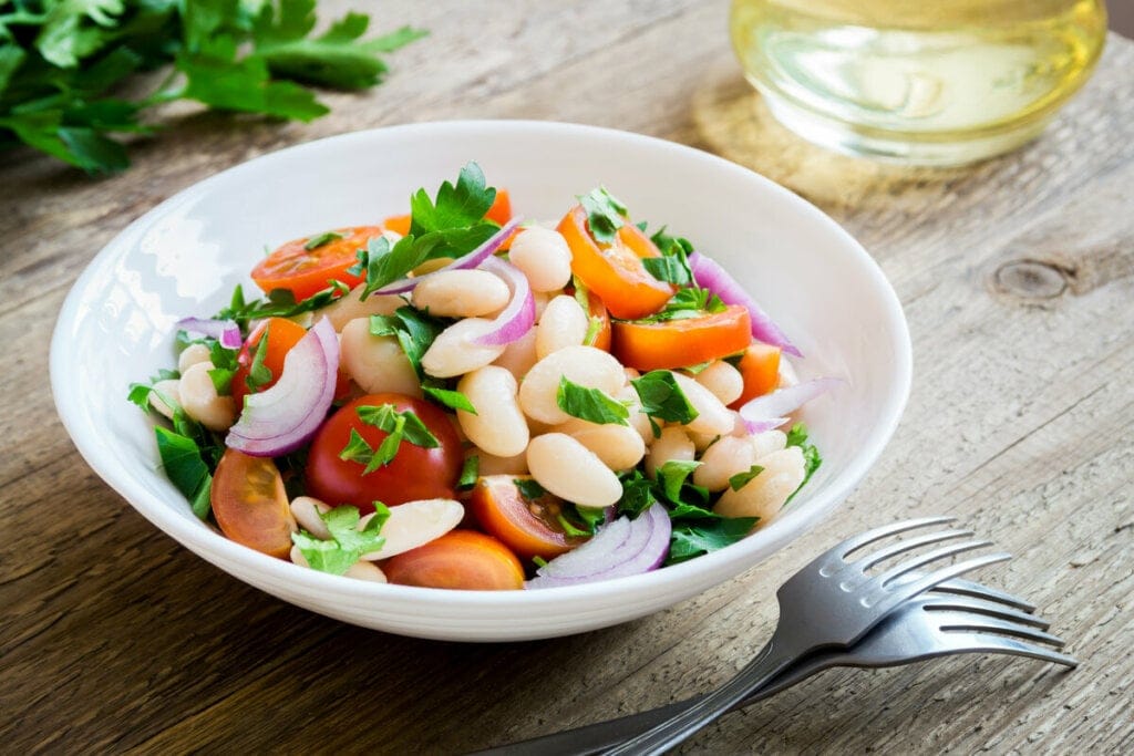 Salada de feijão-branco com tomate e salsa em um prato branco 
