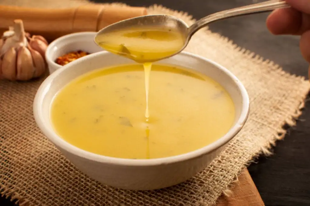 Sopa cremosa de mandioca com uma mão feminina segurando uma colher