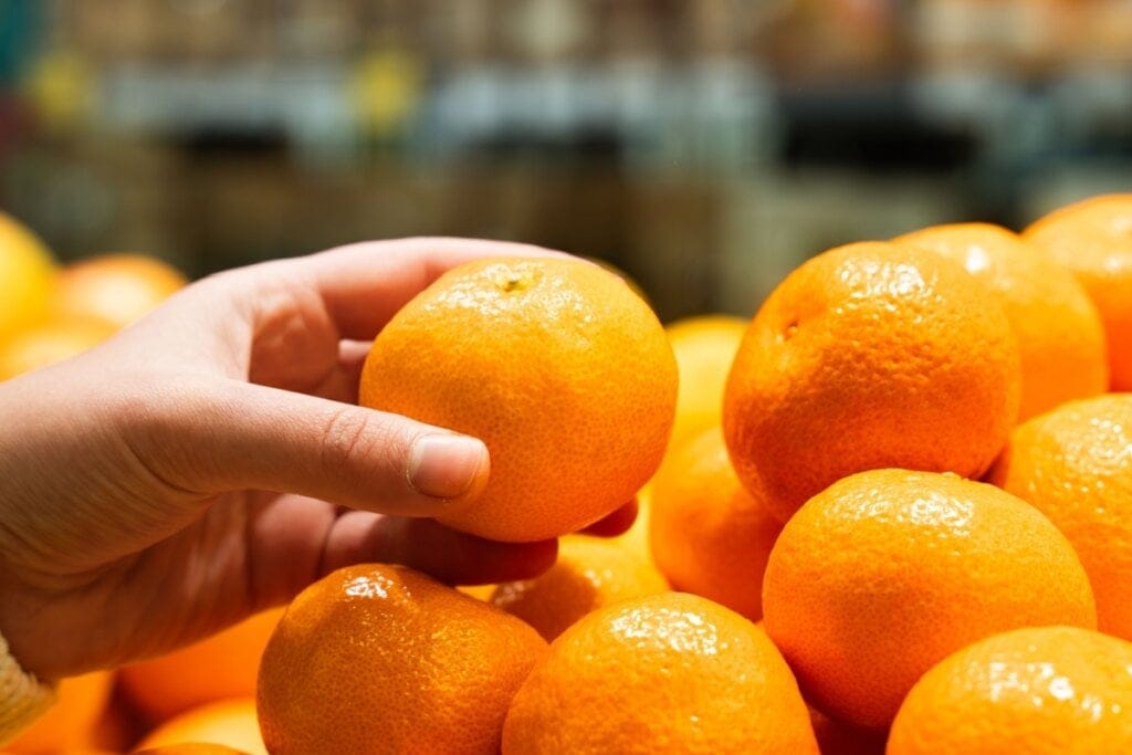 mão segurando tangerina em frente a monte de tangerinas