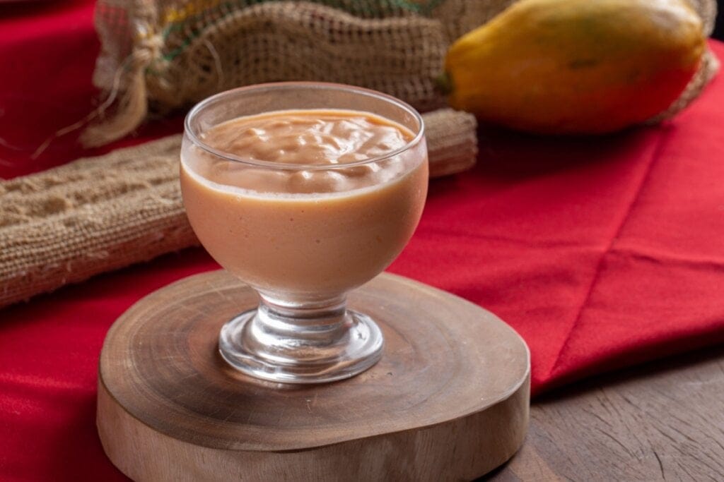 Mousse de mamão em uma taça de vidro em cima de uma tábua de madeira com um mamão inteiro do lado