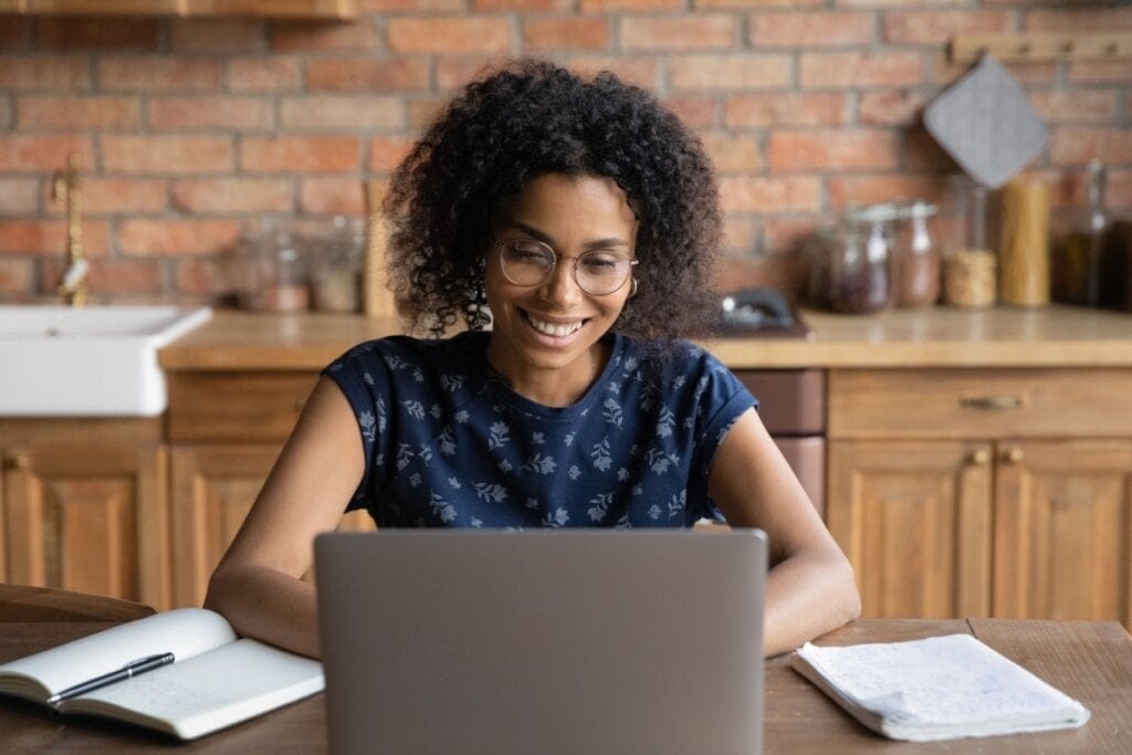 Mulher jovem sentada em frente ao notebook estudando e sorrindo