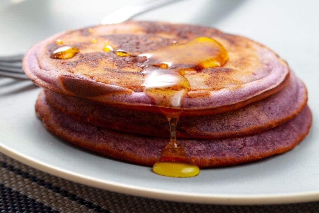 Três panquecas de açaí empilhadas em um prato branco com mel