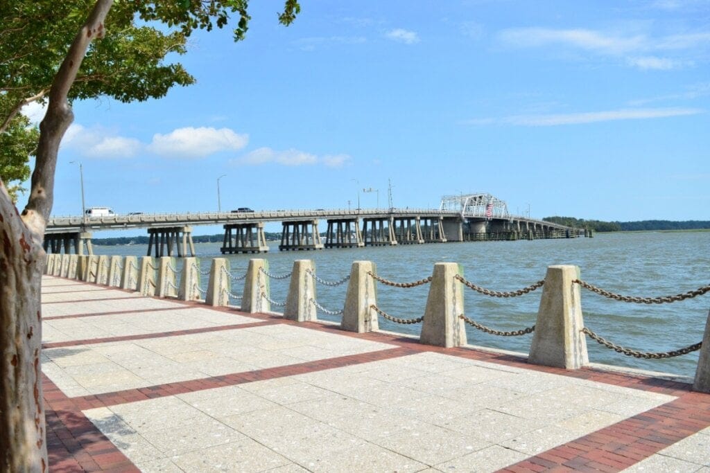 Calçadão ao lado do mar e ao fundo uma ponte