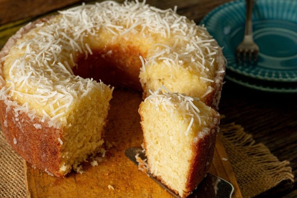 Bolo de coco servido em cima de tábua de madeira em cima de mesa de madeira