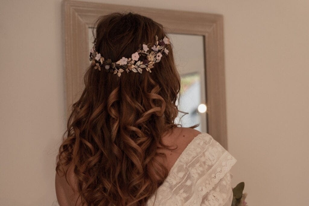 Mulher vestida de noiva com o cabelo preso na parte de cima com um arranjo floral, com o cabelo castanho e cacheado