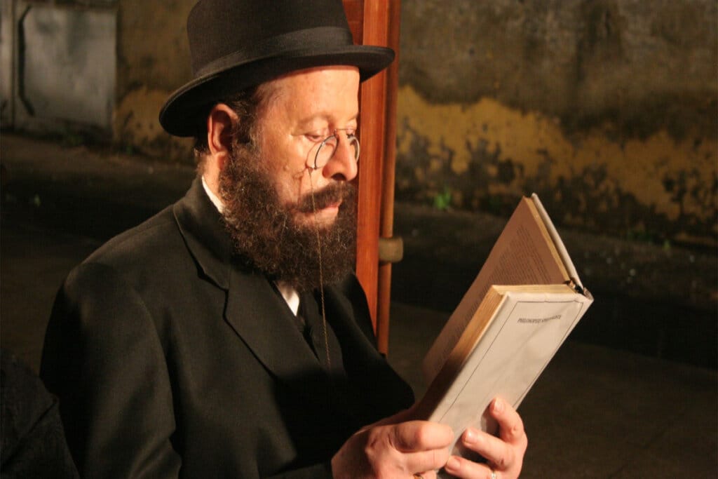 homem de barba, roupa e chapéu pretos e óculos lendo livro