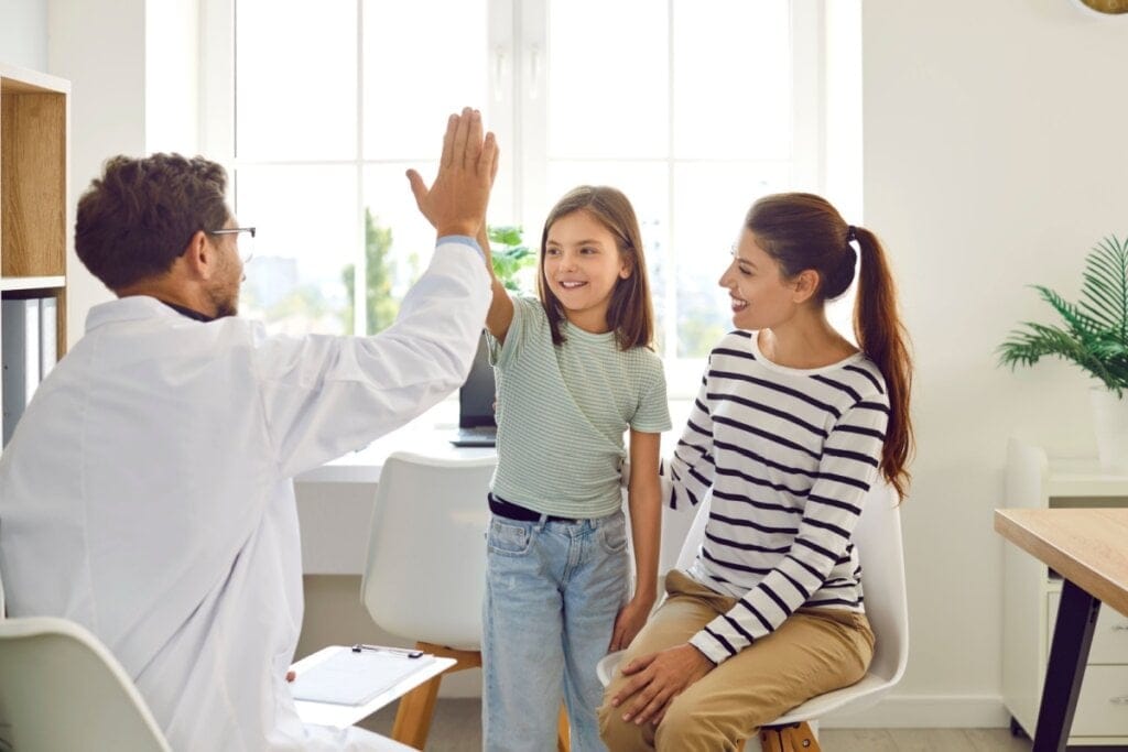 Médico fazendo um hi five com uma criança ao lado de uma mulher, todos sentados