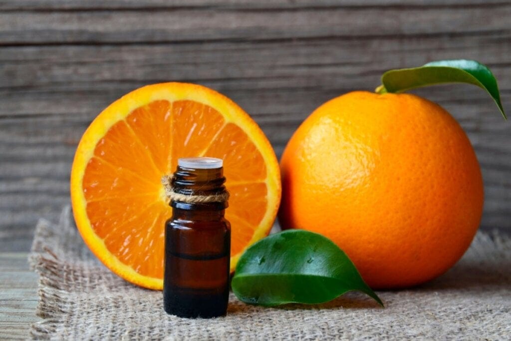 óleo essencial de laranja ao lado de uma laranja inteira e outra cortada ao meio em cima de mesa de madeira