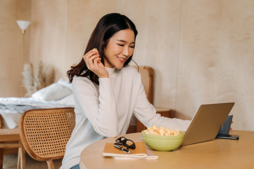 Mulher sentada assunto algo em um notebook e comendo pipoca