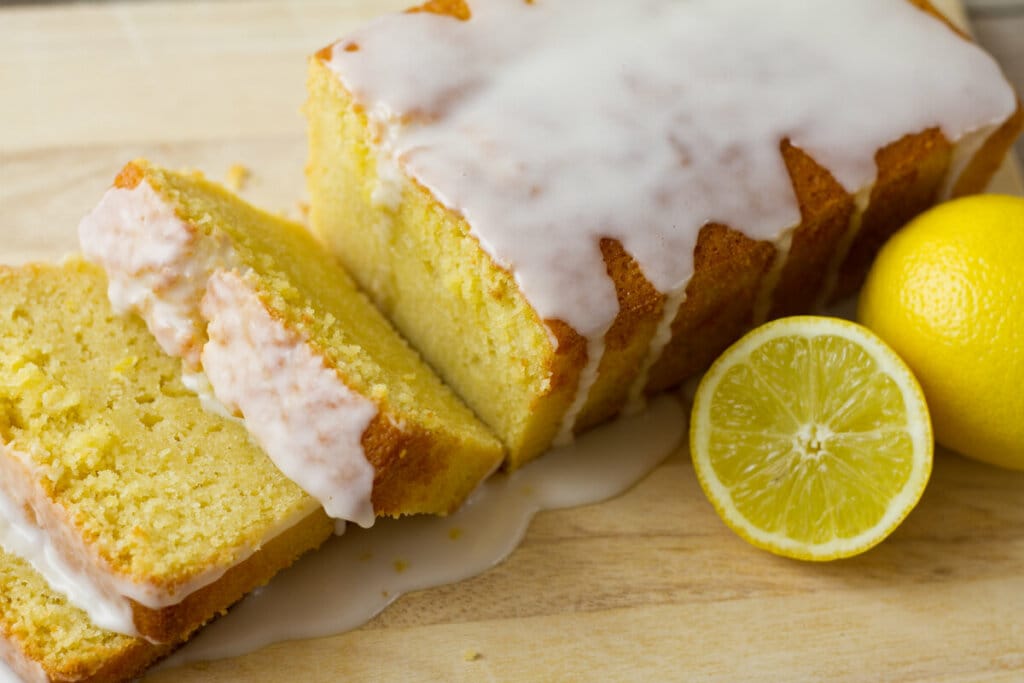 Bolo de limão com calda com dois pedaços cortados em cima de uma mesa de madeira com rodelas de limão