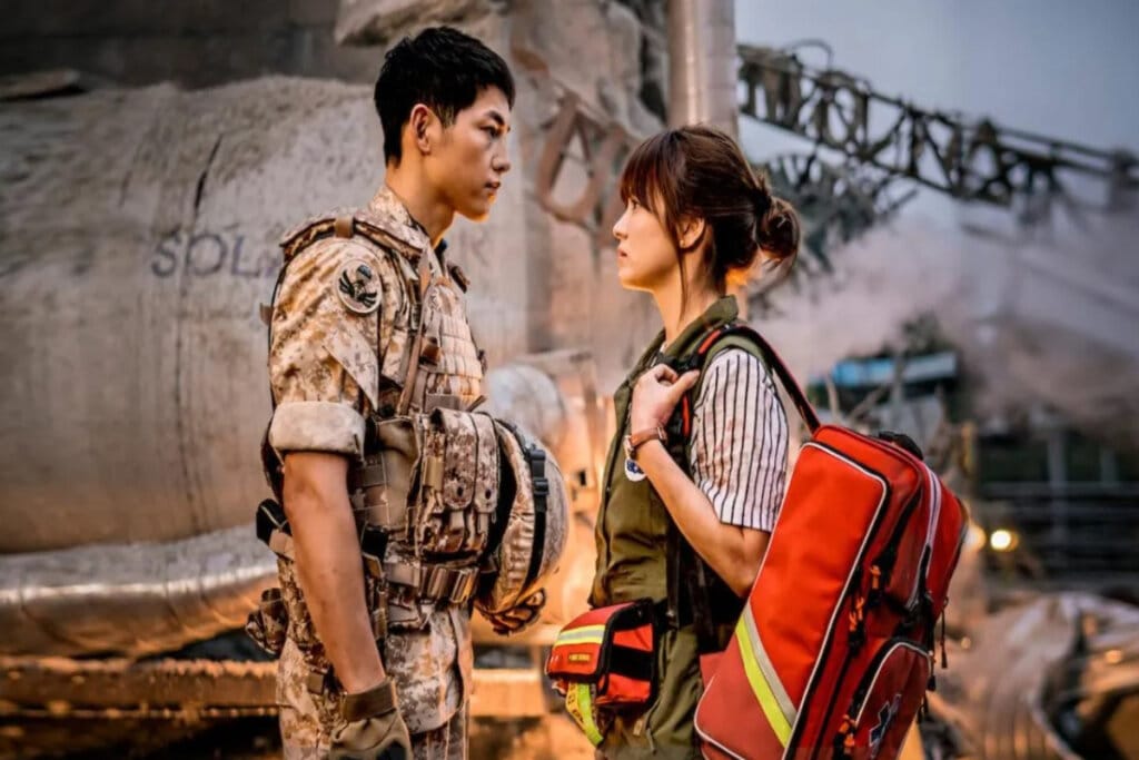 Imagem de um homem com roupa de soldado de frente para uma mulher usando roupas e equipamentos de resgate ao fundo uma construção destruída