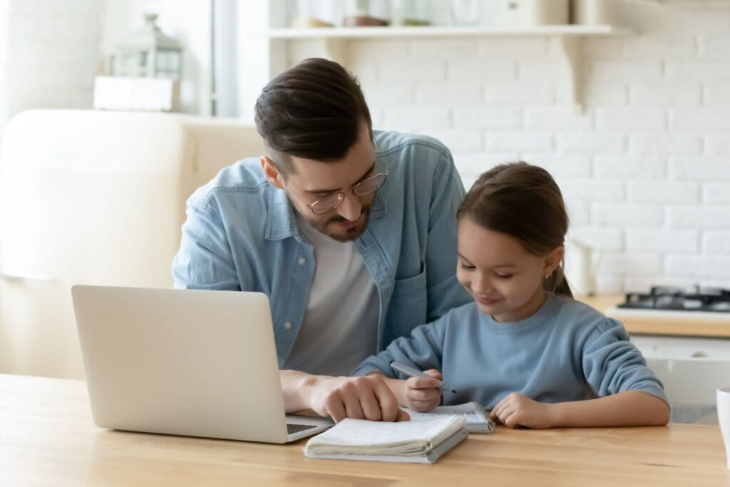 Homem e menina sentados lado a lado e ela escrevendo em um caderno 