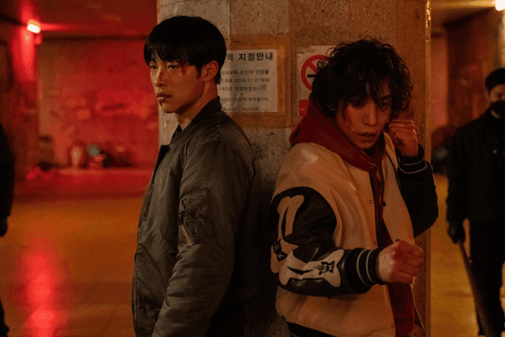 Dois homens parados atrás de poste com o rosto machucado usando roupas de frio 