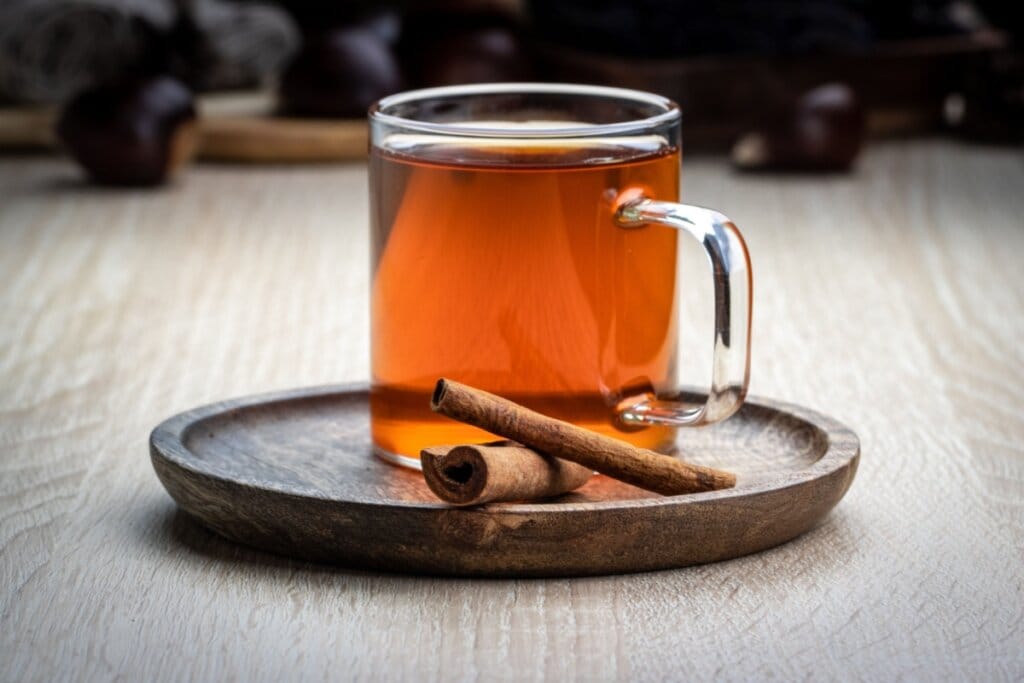 Chá de espinheira-santa com canela em caneca de vidro e em cima de um recipiente de madeira 