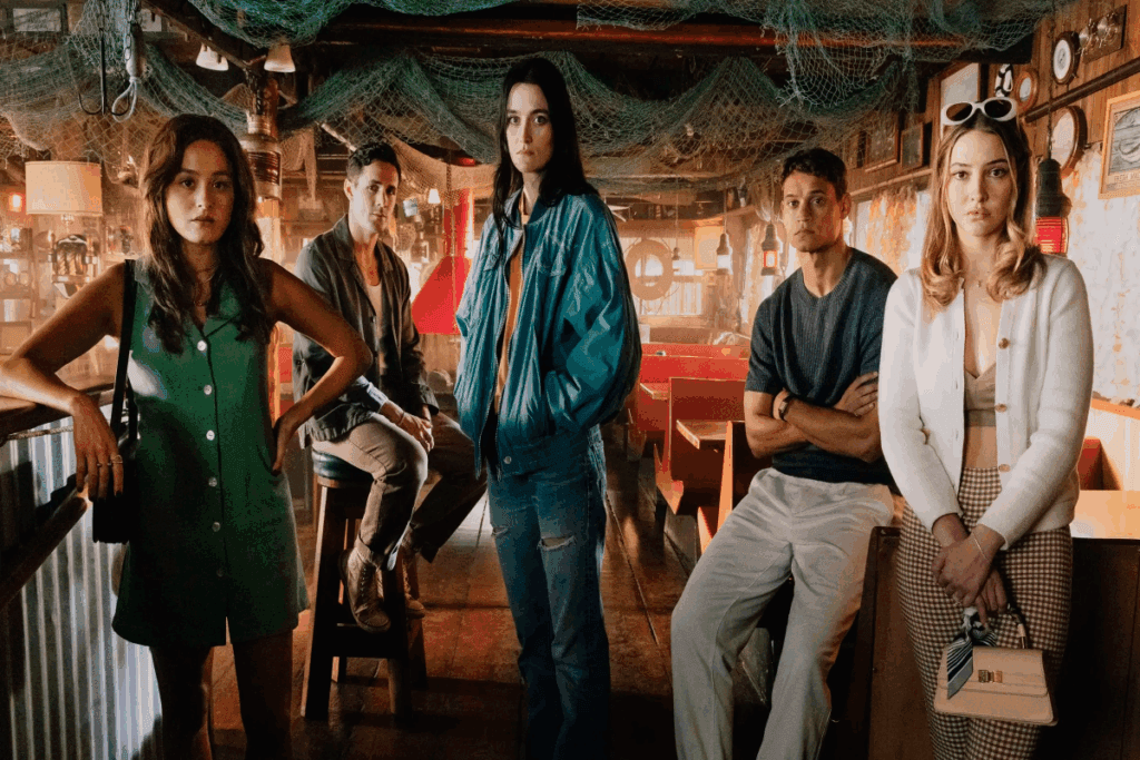 4 pessoas sentadas em bar, três mulheres estão de pé e dois homens sentados 