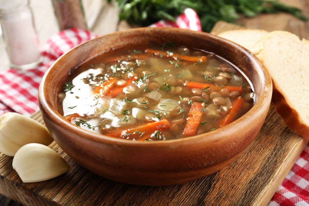 Sopa de lentilha com cenoura servida em tigela de madeira em cima de mesa de madeira