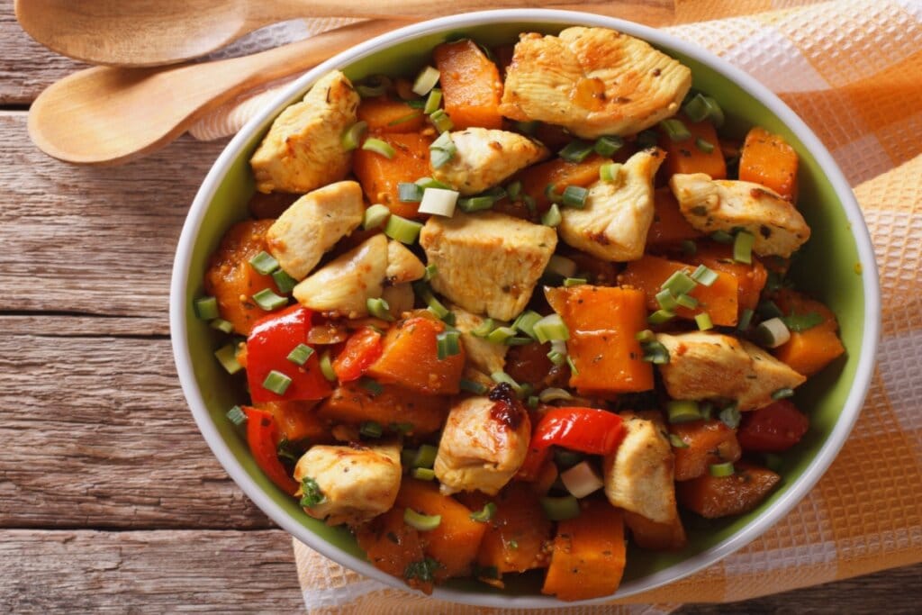 Tigela com ensopado de frango em cubos, batata-doce em pedaços e pimentão vermelho, finalizado com cebolinha picada