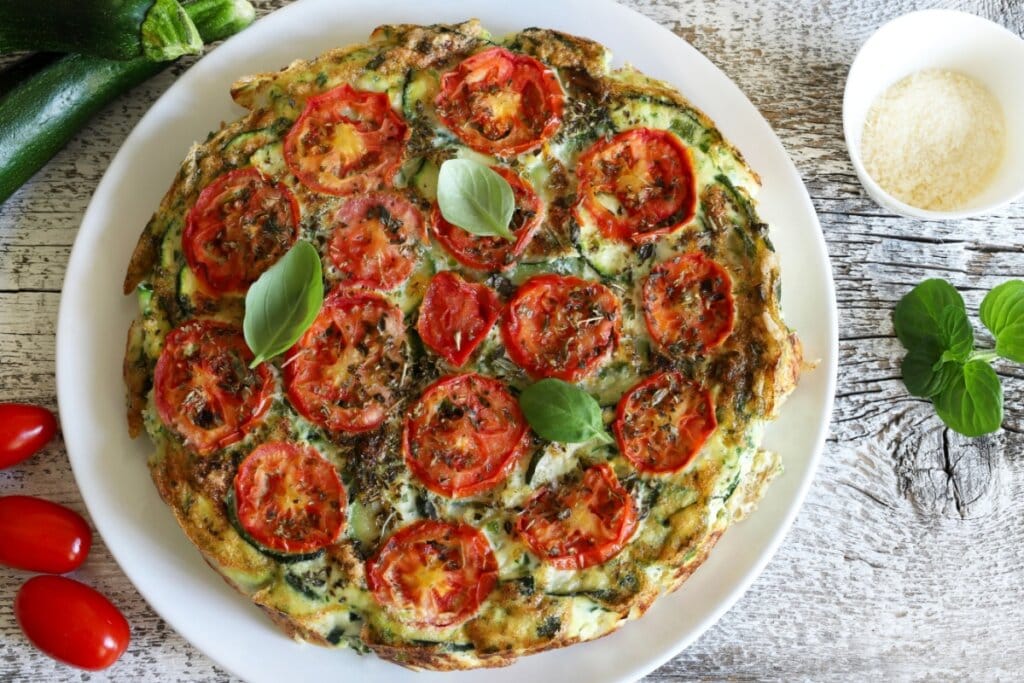 Prato branco com fritada de abobrinha e tomate decorada com folhas de manjericão