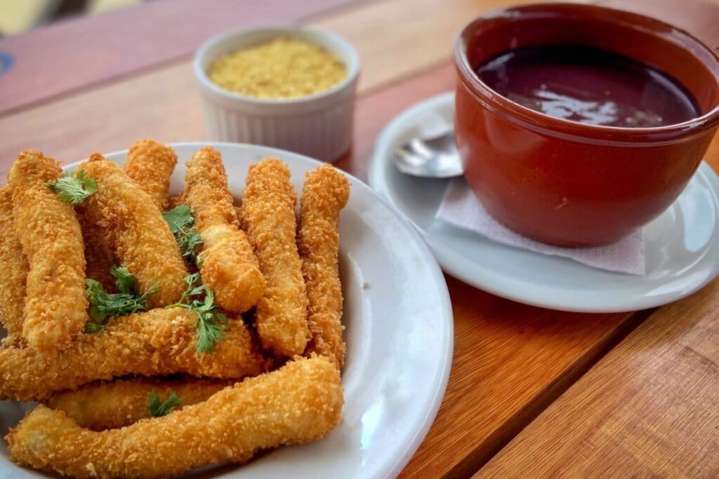 Prato com peixe empanado e recipiente marrom com creme de açaí em cima de uma mesa de madeira 