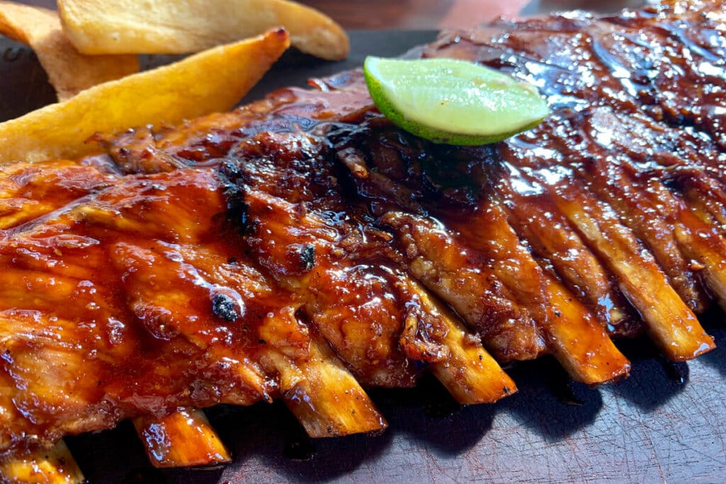 Costela com molho barbecue em cima de uma superfície preta e com a fatia de um limão em cima