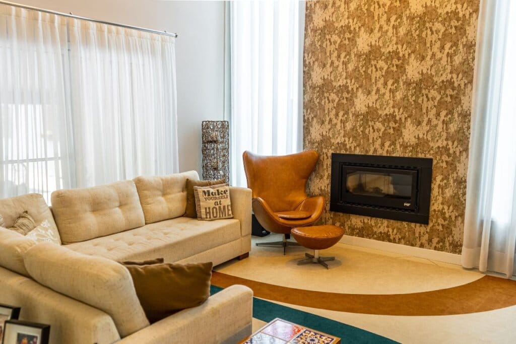 Sala de estar com janela com cortina branca, sofá na mesma cor e lareira