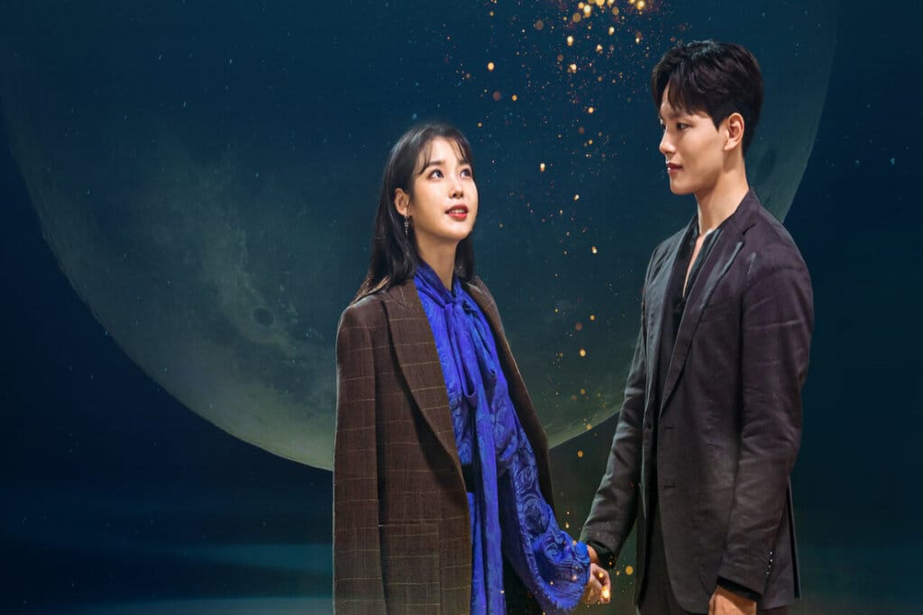 personagens principais de "Hotel Del Luna" de mãos dadas e em frente a ilustração da Lua 