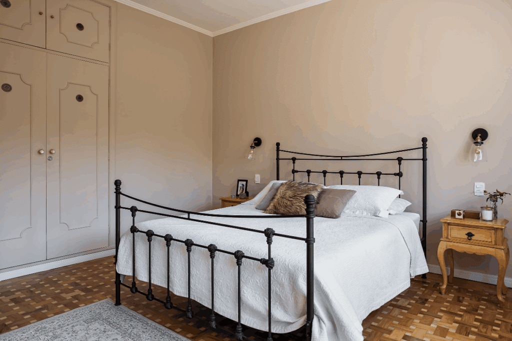 Quarto com paredes em bege, com cama de casal de ferro preta e com roupas de cama em branco e almofadas em tons de marrom e com armario planejado