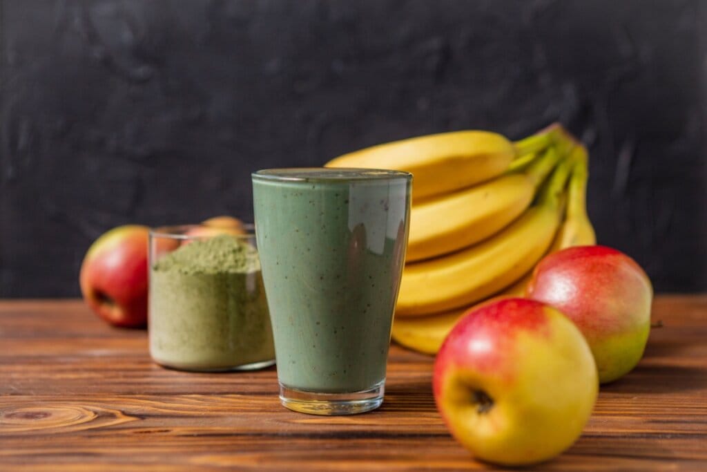 Vitamina de matcha com banana e maçã servido em copo de vidro em cima de mesa de madeira