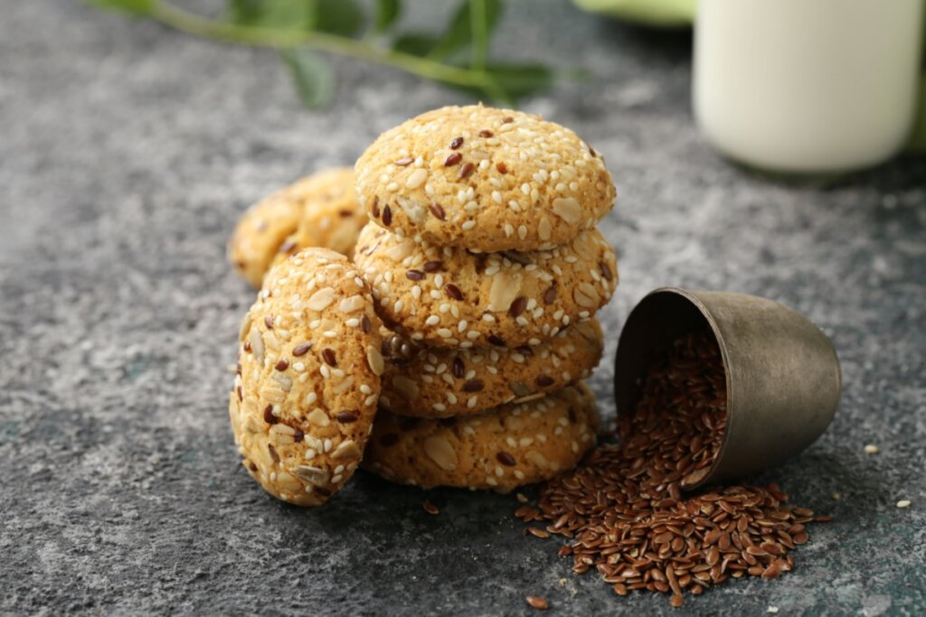 imagem de quatro cookies com linhaça empilhados e potinho com sementes de linhaça caído ao lado