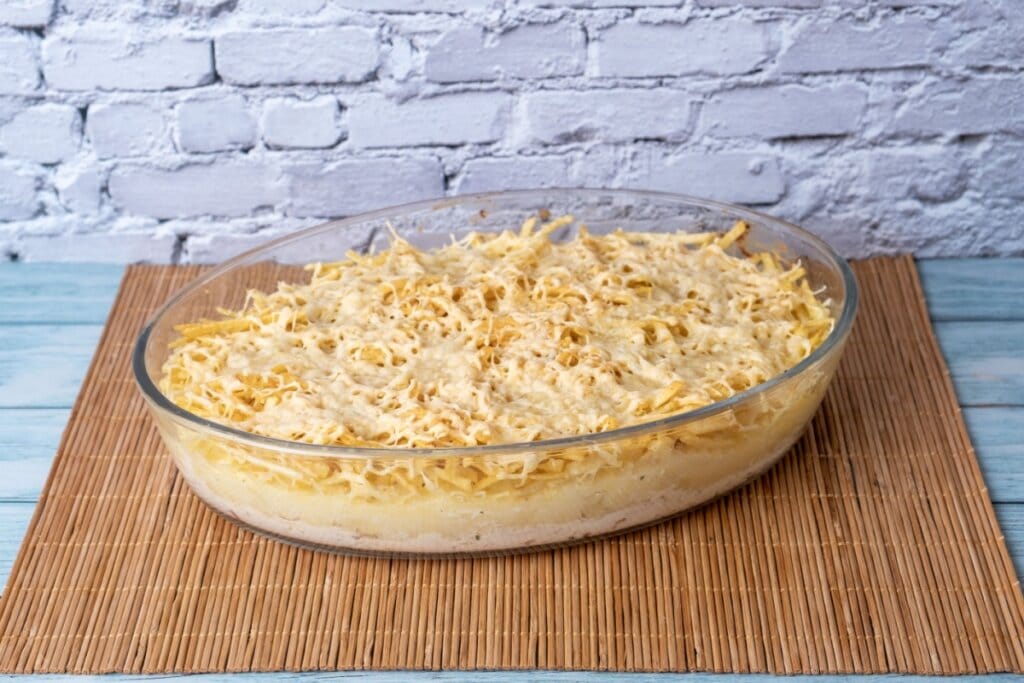 recipiente de vidro com fricassê de frango com batata palha e queijo em cima de superfície de madeira