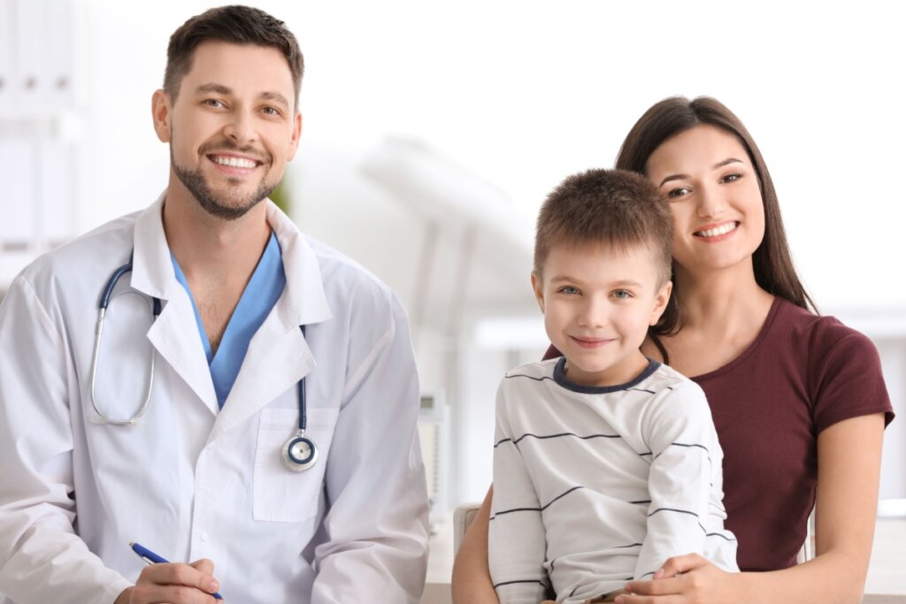 Médico sorrindo ao lado de uma mãe e seu filho em consulta