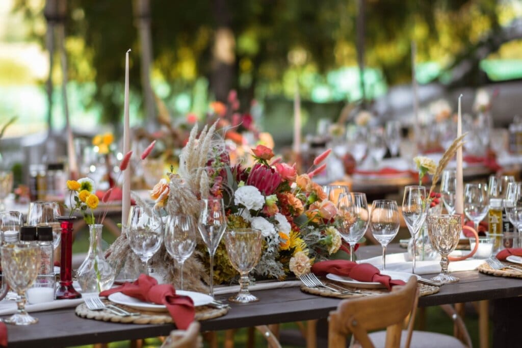 Mesa de jantar de casamento decorada com flores em diferentes tons, pratos brancos com guardanapo de pano em mesa de madeira ao ar livre