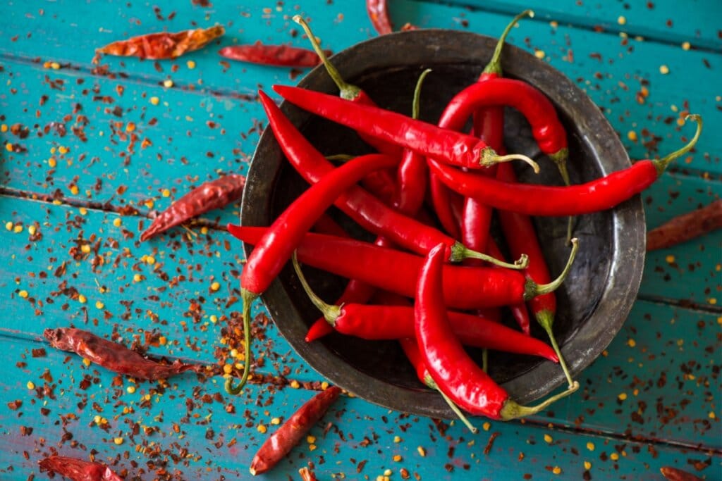 Porção de pimenta vermelha dentro de pote marrom e pimenta calabresa espalhada em volta