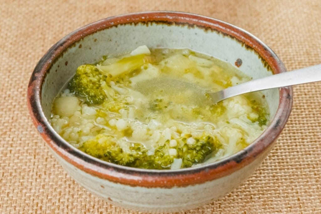 Sopa de brócolis com couve-flor servida em tigela de cerâmica em cima de mesa de madeira