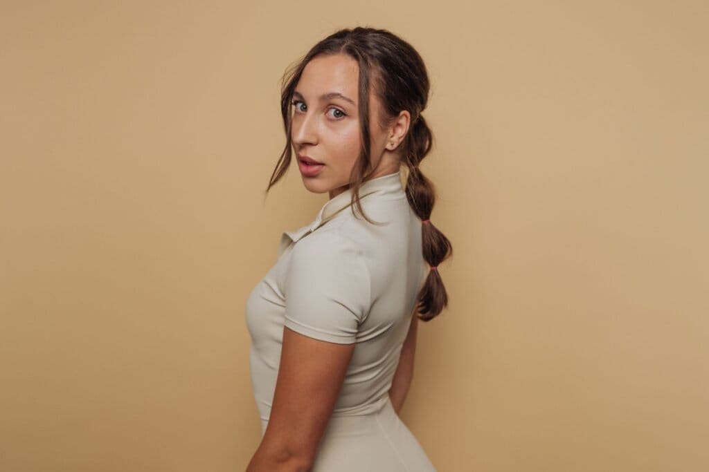 Mulher, em frente a um fundo bege, virada de lado mostrando a trança bolha no cabelo