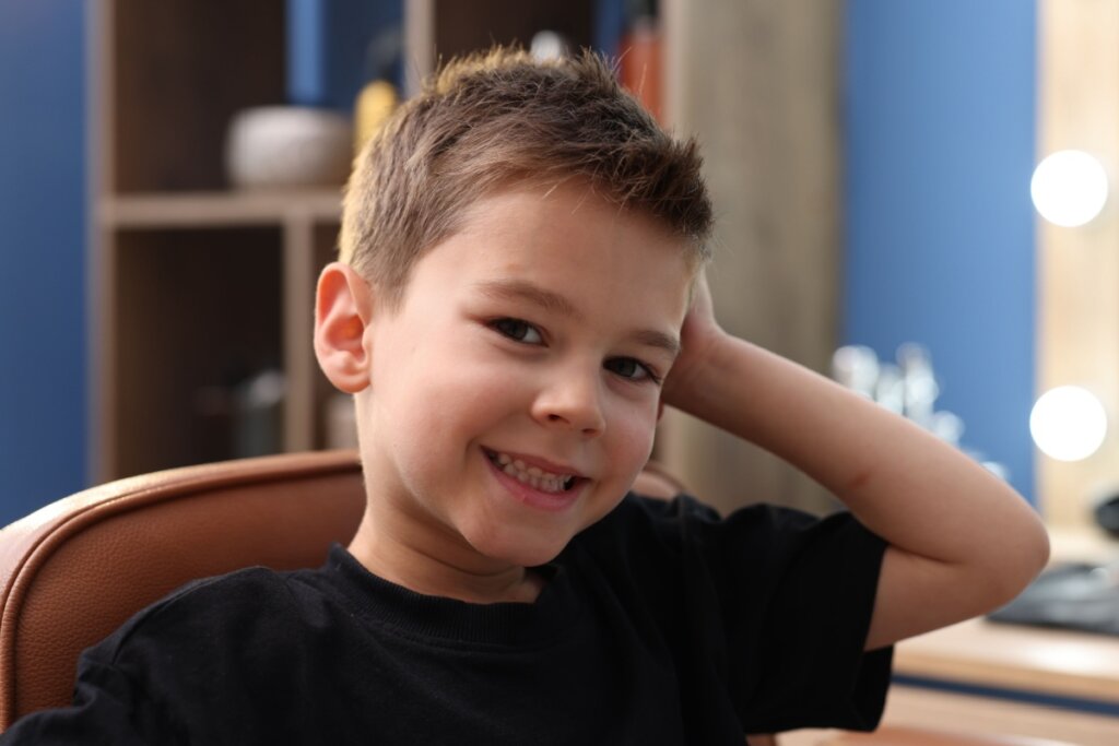 Menino com cabelo curto e repicado, usando camiseta preta em barbearia