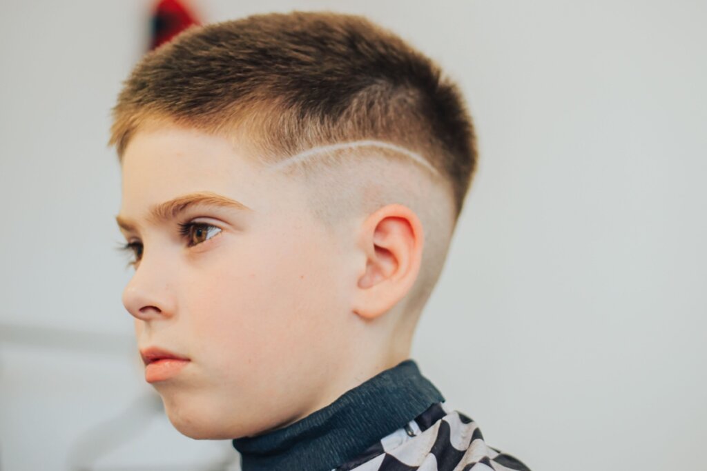 Menino com o cabelo curto e com risca na lateral em barbearia