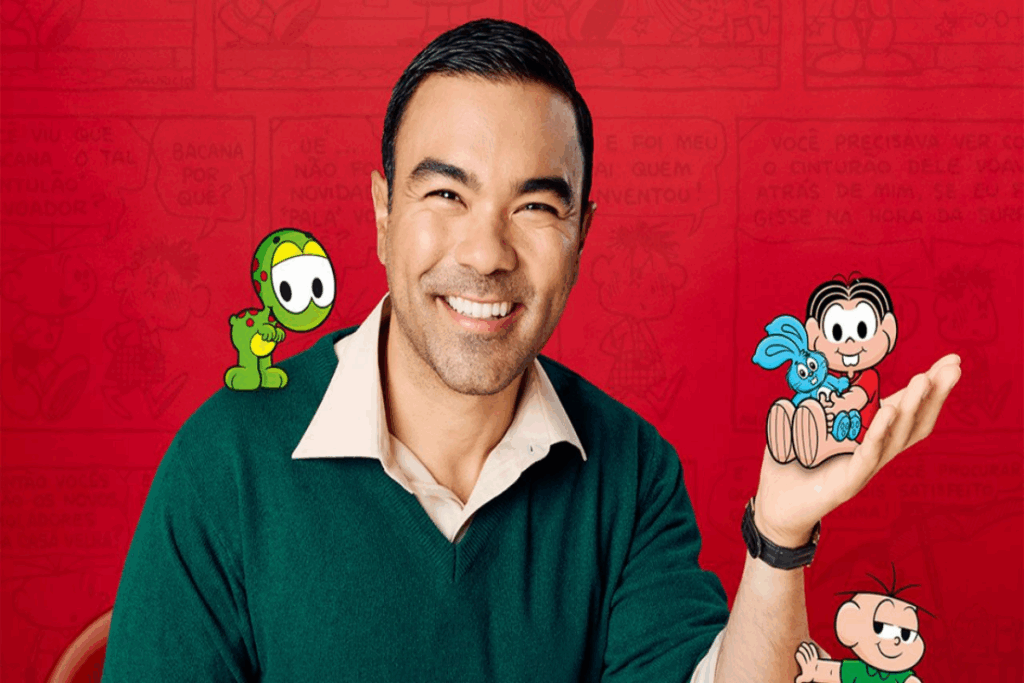 Homem com cabelo curto, usando camisa com bola branca e suéter verde com personagens da Turma da Mônica no ombro e na mão e no braço