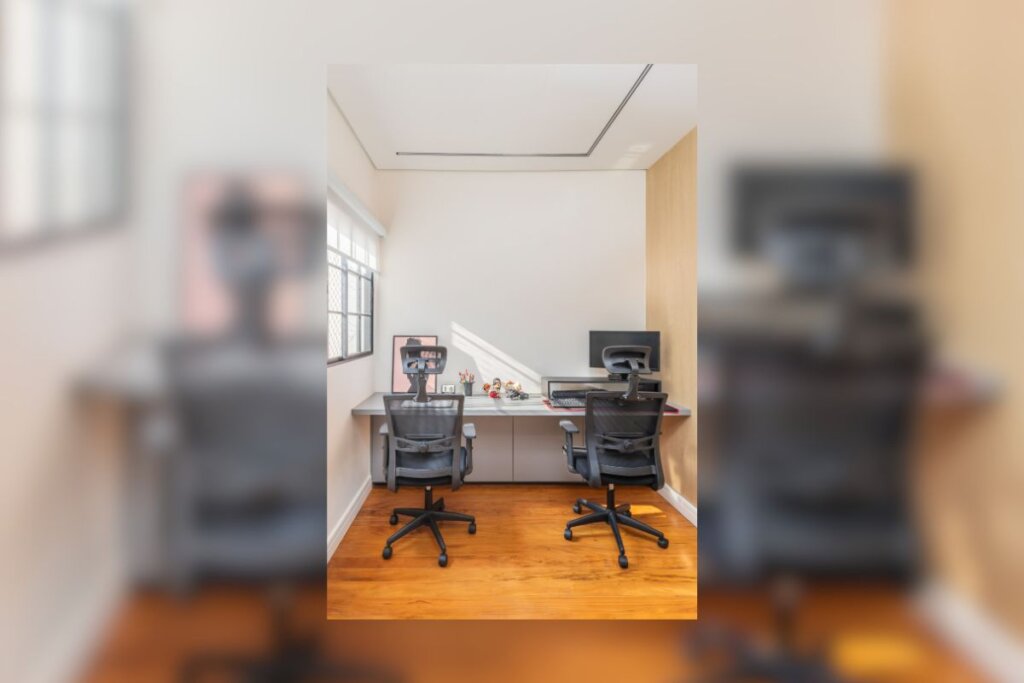 Sala com uma mesa branca, duas cadeiras pretas e dois computadores em frente a elas