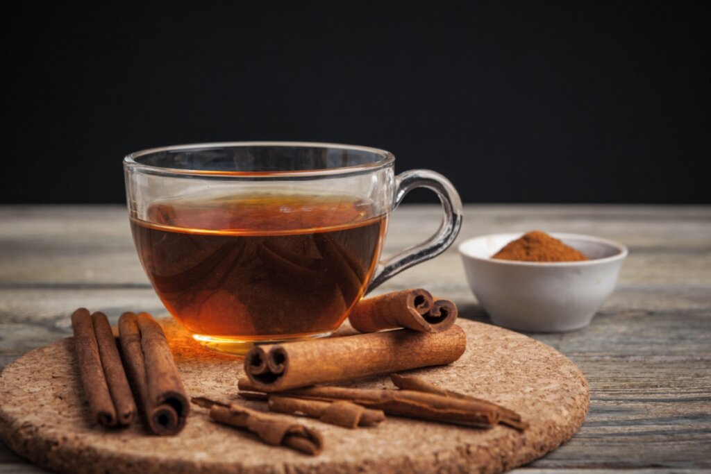 xícara de vidro com chá de canela em cima de uma bandeja redonda e pedaços de canela ao redor. 