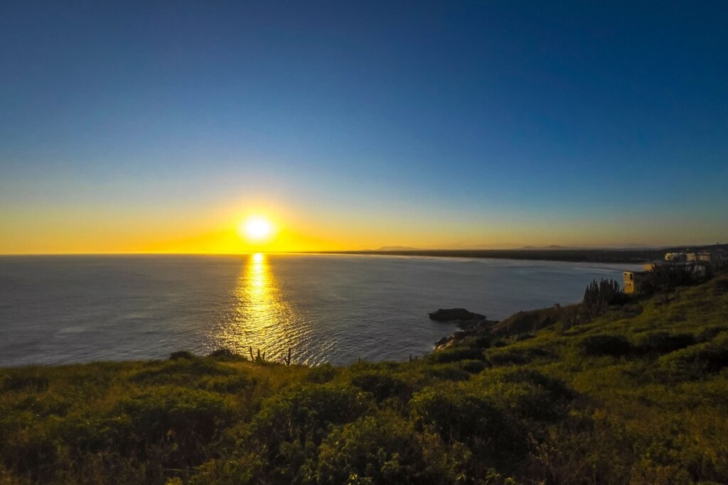 Pôr do sol em uma praia em Arraial do Cabo com o mar na frente de um monte com grama 
