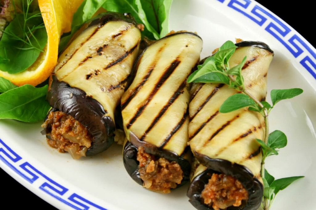 Rolinho de berinjela com carne moída com vegetais e em prato branco e azul 
