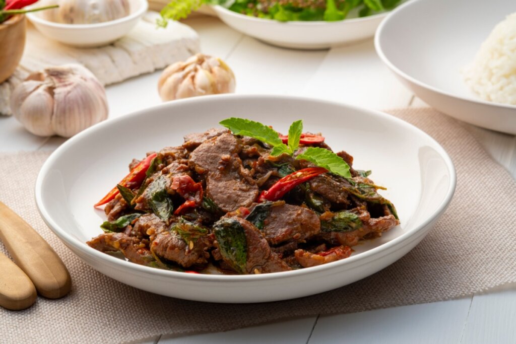 Prato branco com carne com pimenta vermelha e folhas de manjericão