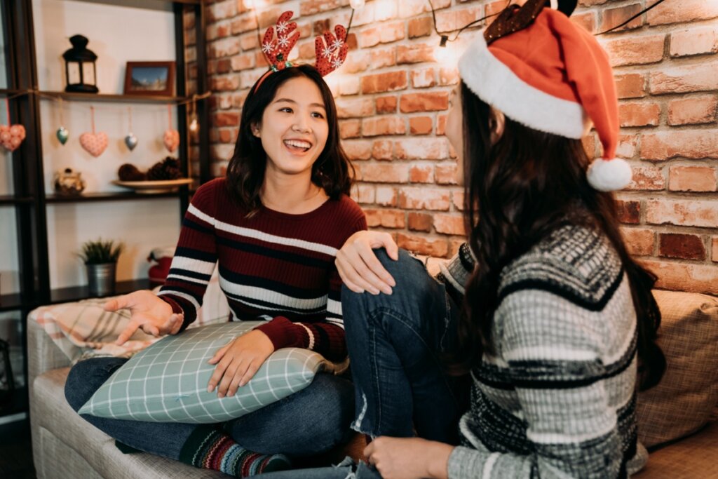 Duas jovens sentadas em sofá conversando usando adereços natalinos na cabeça 